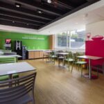 Spacious cafeteria with a minimalist design, featuring colorful chairs and tables, ready for dining.